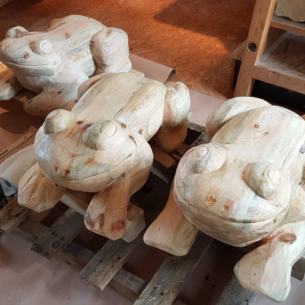 Drei ausgearbeitete Froschskulpturen aus Holz nebeneinander in der Werkstatt.