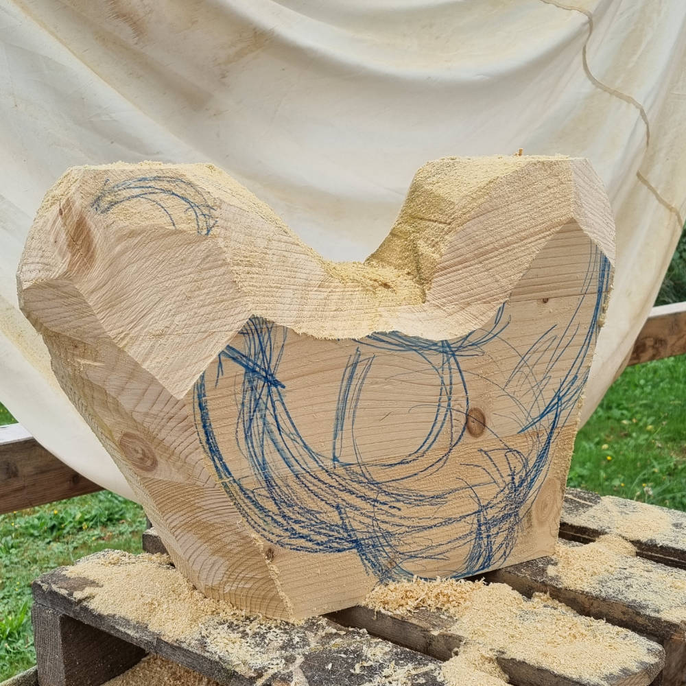 Holzblock mit aufgezeichneter Hühnerform und ersten groben Sägeschnitten als Vorlage für die weitere Bearbeitung.