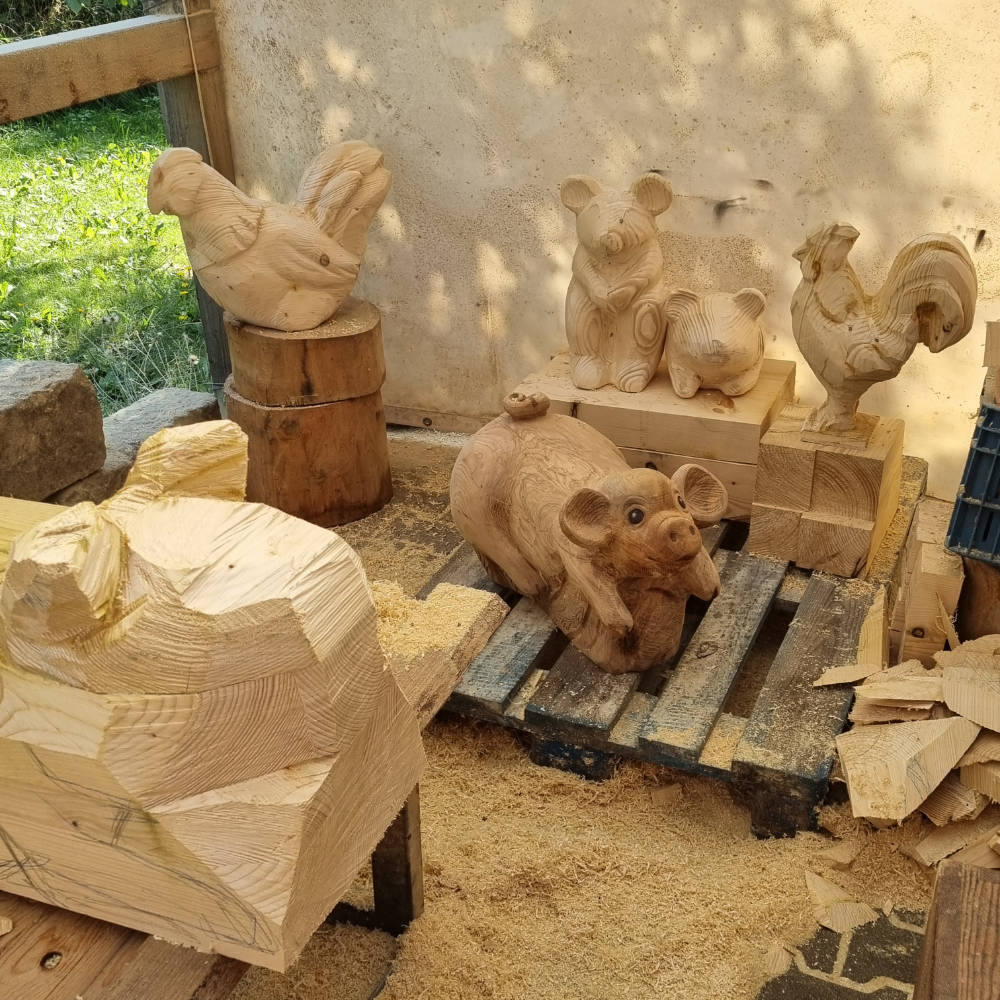 Hühnerskulptur aus Holz zwischen weiteren ausgearbeiteten Tierskulpturen.