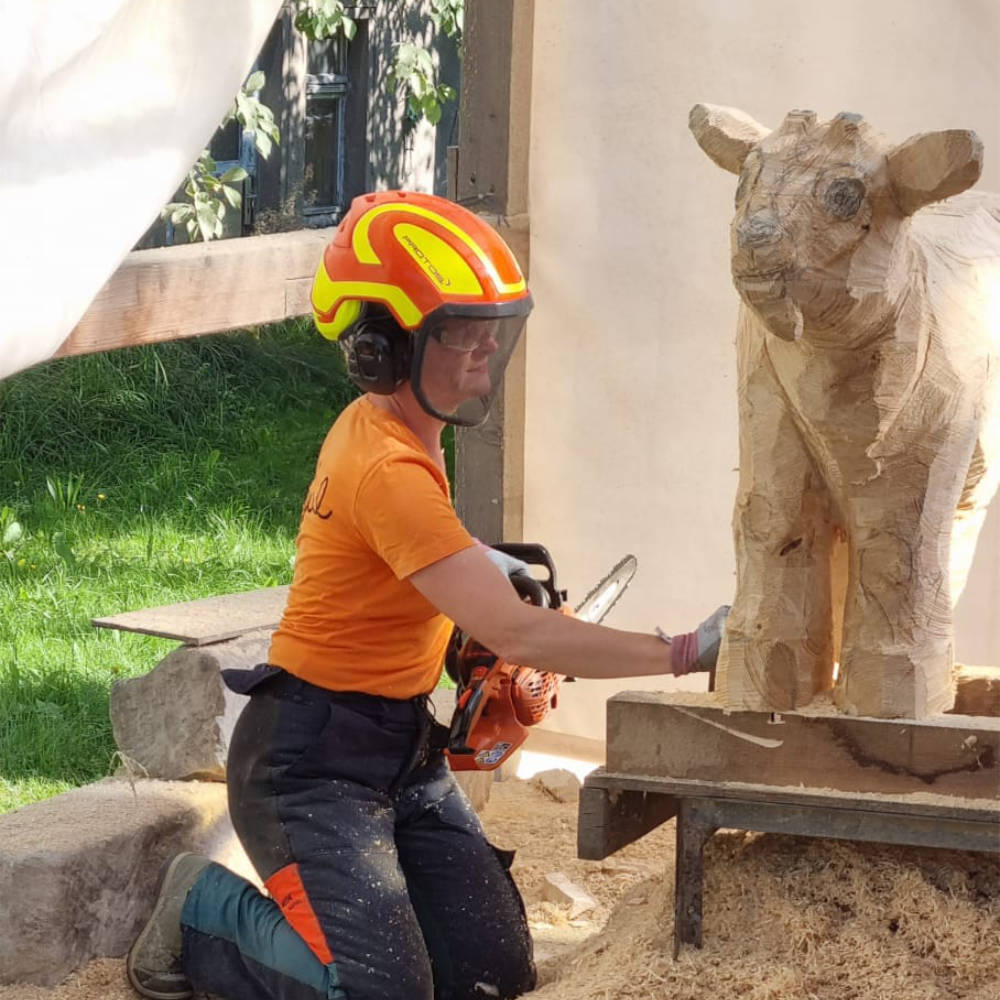 Juliane Uebe bearbeitet eine Kuhskulptur aus Holz durch grobe Schnitzarbeiten.