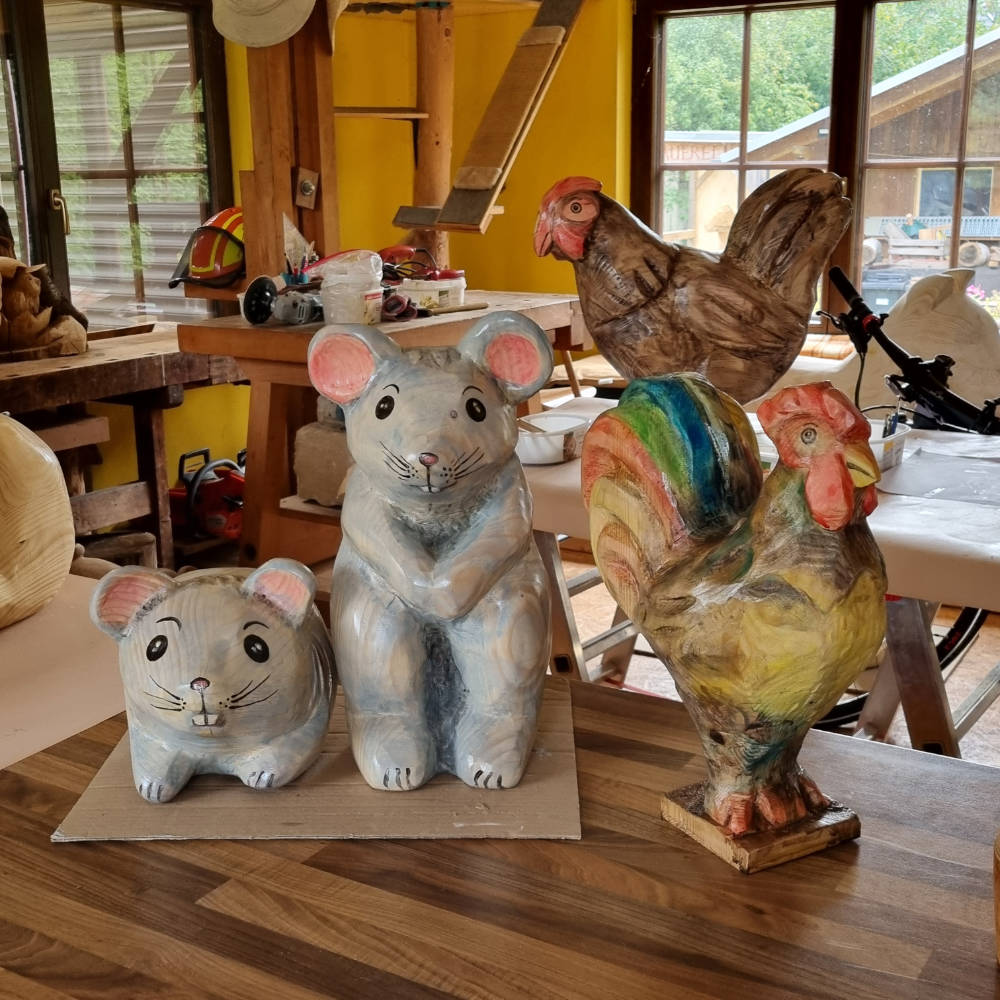 Bemalte Hühnerskulptur aus Holz mit weiteren fertig gestalteten Tierskulpturen in der Werkstatt.