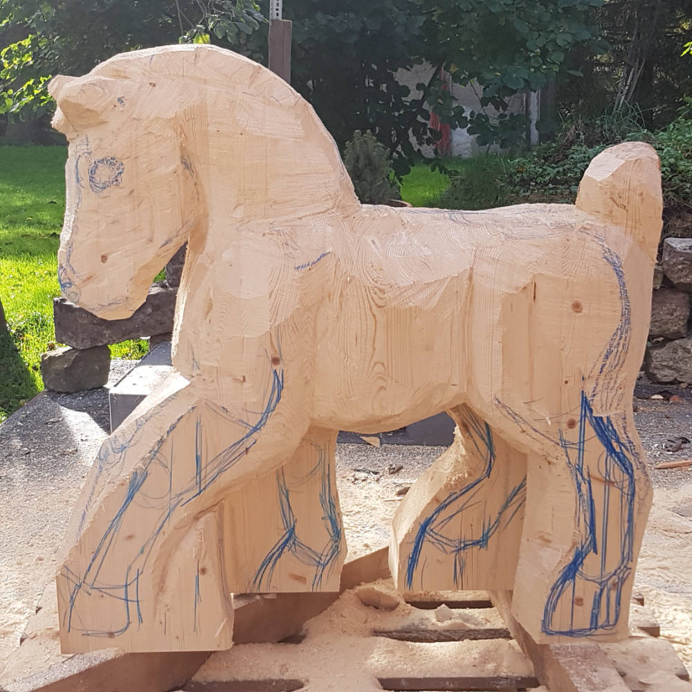Fortgeschrittene Bearbeitung einer Holzskulptur: Der Kopf des Pferdes wurde grob aus dem Holzblock herausgearbeitet.