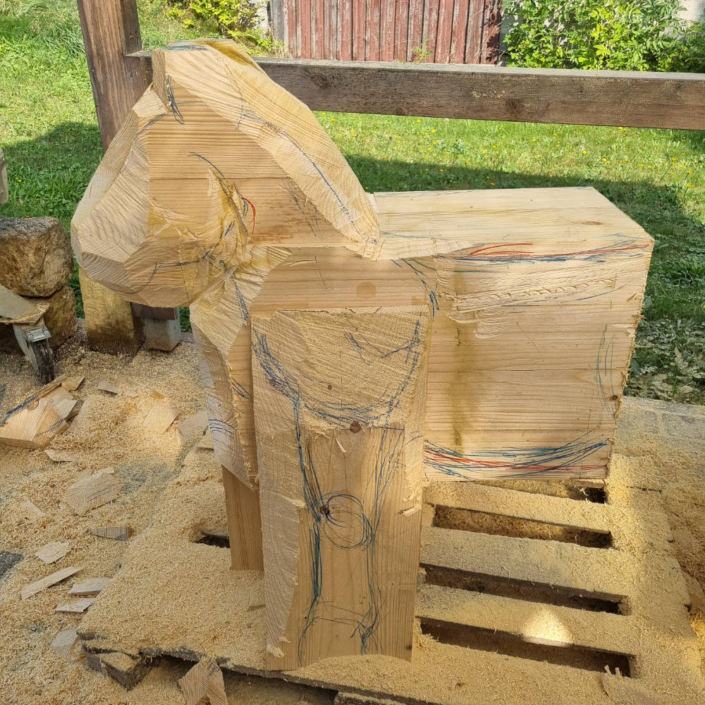 Grob aus einem Holzblock herausgearbeitete Pferdeform.