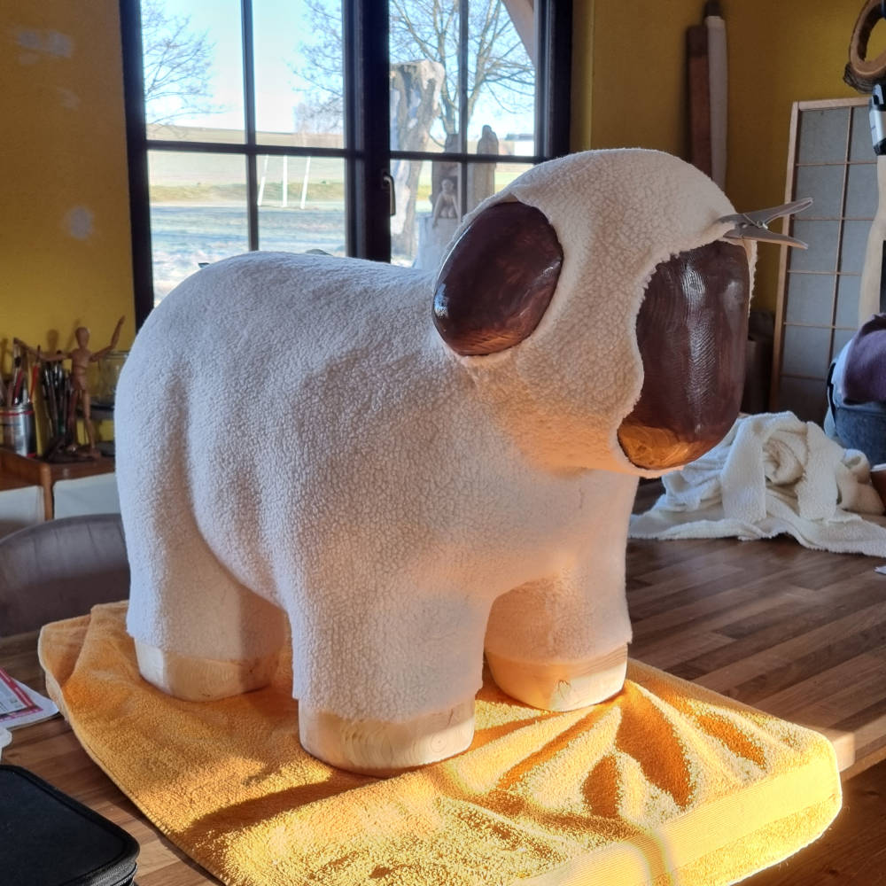 Fast fertig ausgearbeitete Schafskulptur aus Holz mit noch fehlender Bemalung der Gesichtszüge in der Werkstatt.
