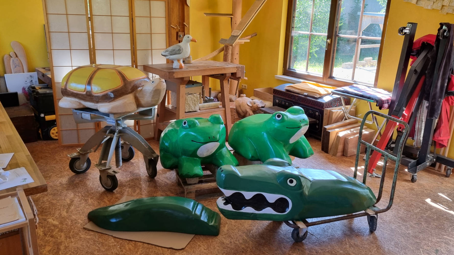 Werkstattraum mit verschiedenen Tierfiguren aus Holz, darunter Schildkröten, Frösche und ein Krokodil.