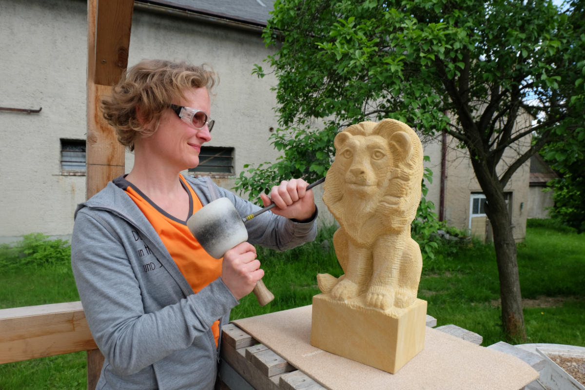 Juliane Uebe arbeitet an einer sitzenden Löwenskulptur aus Sandstein.