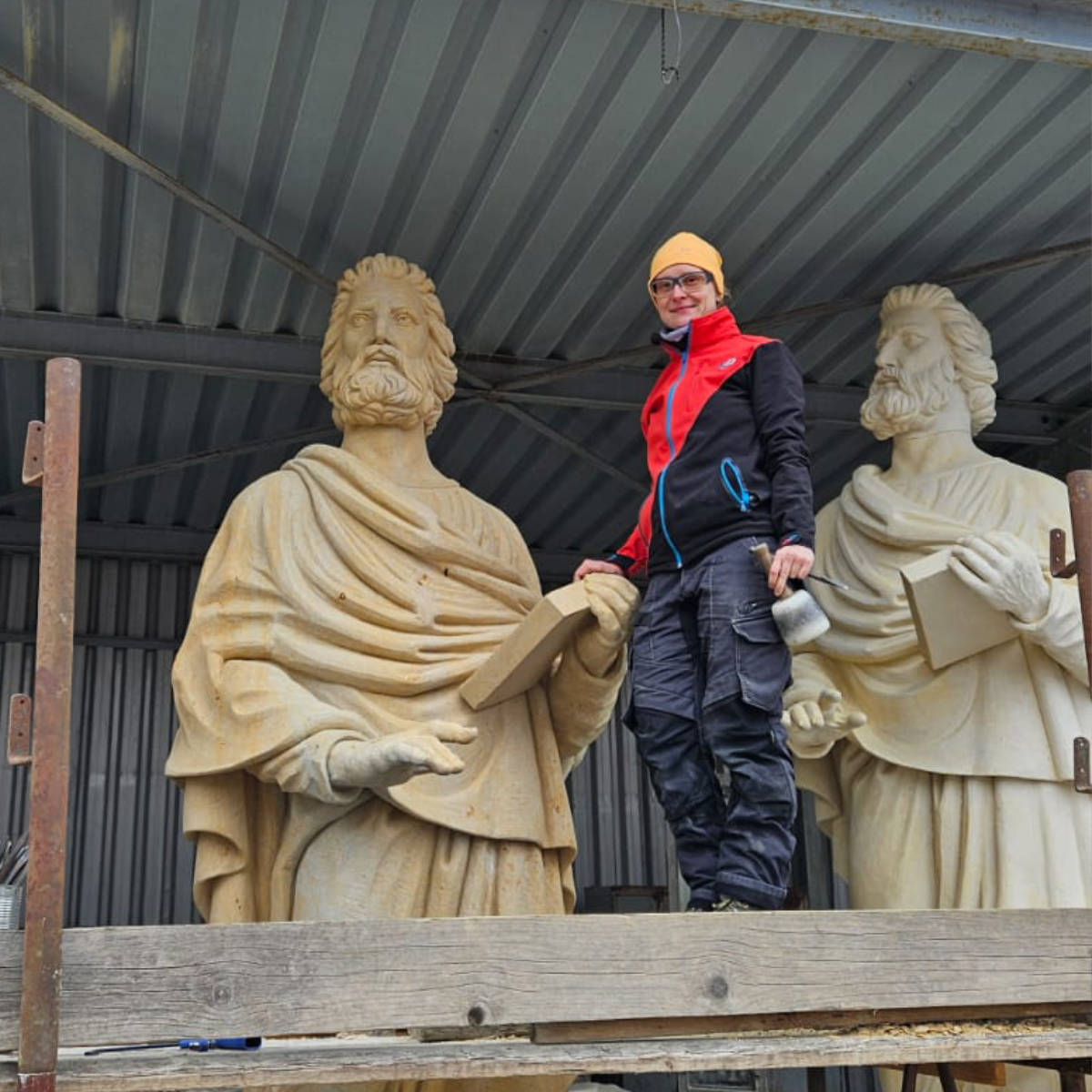 Juliane Uebe steht neben der Sandsteinstatue des Propheten Hosea und zeigt im Größenvergleich die Dimension der 3,3 Meter hohen Skulptur.